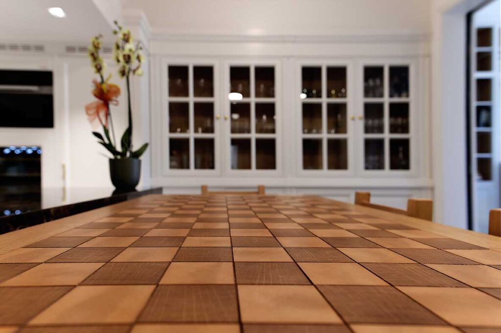 Tavolo in legno massello con dettagli in legno a quadri, situato in un ambiente elegante con grandi finestre e piante decorative. Arredamenti Fagnini – Arredo su misura per spazi esclusivi, con mobili personalizzati in legno, arte artigianale e design contemporaneo a Firenze | Blog 2026/1 - Il Su Misura nel Lusso Contemporaneo: Quando l’Arredo Diventa Identità | Blog Arredamenti Fagnini Firenze - Arredamenti Fagnini s.r.l. Via Pistoiese 247/A - 50145 Firenze (FI)