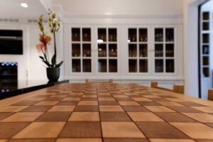 Tavolo in legno massello con dettagli in legno a quadri, situato in un ambiente elegante con grandi finestre e piante decorative. Arredamenti Fagnini – Arredo su misura per spazi esclusivi, con mobili personalizzati in legno, arte artigianale e design contemporaneo a Firenze | Blog 2026/1 - Il Su Misura nel Lusso Contemporaneo: Quando l’Arredo Diventa Identità | Blog Arredamenti Fagnini Firenze - Arredamenti Fagnini s.r.l. Via Pistoiese 247/A - 50145 Firenze (FI)